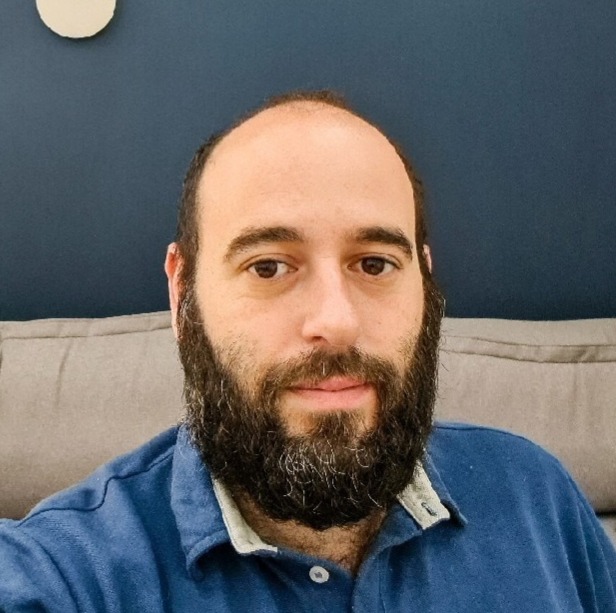 Foto de Lucas Leite, com barba sentado em um sofá, diante de uma placa que diz Nchemi